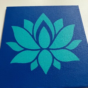 May include: A square canvas painting featuring a teal lotus flower design on a deep blue background. The lotus flower is centered and rendered in a simplified, stylized form. The canvas has a textured surface.