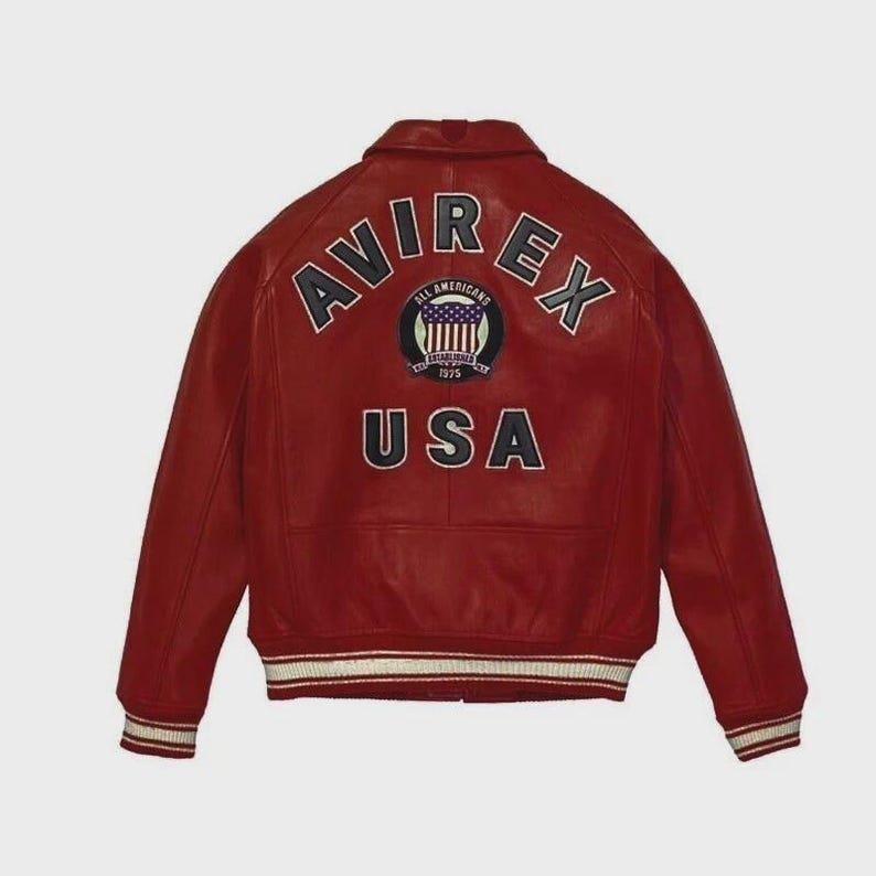Puede incluir: Chaqueta de cuero roja con la palabra "AVIREX" en letras azul marino en la espalda. Debajo, un parche con las palabras "ALL AMERICANS" y "ESTABLISHED 1975". La palabra "USA" est&aacute; debajo. La chaqueta tiene pu&ntilde;os a rayas blancas y azul marino.