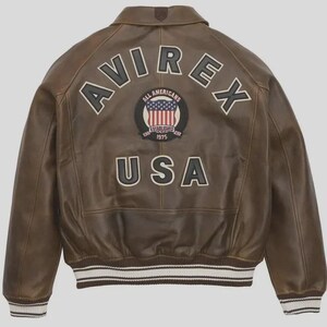 Puede incluir: Chaqueta de cuero marr&oacute;n con la palabra "AVIREX" en los hombros y "USA" en la parte inferior. Un parche circular en el centro presenta las palabras "ALL AMERICANS" y un dise&ntilde;o de bandera estadounidense. La chaqueta tiene un dobladillo a rayas blanco y marr&oacute;n.