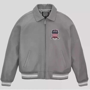 Puede incluir: Chaqueta bomber gris con cuello y cierre de cremallera. La chaqueta presenta un parche en el pecho con un dise&ntilde;o rojo, blanco y azul. Los pu&ntilde;os y el dobladillo tienen detalles a rayas blancas y grises.