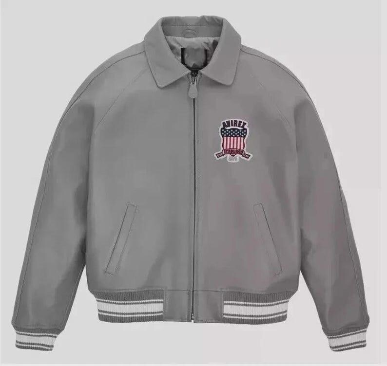 Puede incluir: Chaqueta bomber gris con cuello y cierre de cremallera. La chaqueta presenta un parche en el pecho con un dise&ntilde;o rojo, blanco y azul. Los pu&ntilde;os y el dobladillo tienen detalles a rayas blancas y grises.