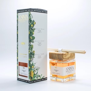 Może przedstawiać: Kwadratowy szklany dyfuzor z drewnianą nakrętką i patyczkami, obok wysokiego pudełka. Butelka zawiera jasno pomarańczowy płyn. Na pudełku i butelce widnieją napisy "ANIMA Mediterranea" i "Giardino dei Cedri".