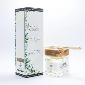 Może przedstawiać: Białe pudełko i szklany słoik z drewnianą pokrywką, oba z napisem "ANIMA MEDITERRANEA". Pudełko zawiera włoski tekst i ilustracje botaniczne. Słoik zawiera przezroczysty płyn i drewniane patyczki.