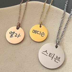 May include: Three gold necklaces with round pendants. The pendants have Korean text on them. The text on the pendants reads "Ella", "Madison", and "Steven".
