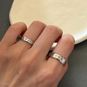 May include: Two silver rings with engraved Korean text. The ring on the left has a heart symbol and the text "마이 풀". The ring on the right has the text "핀 버튼".