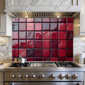 May include: A red and black tile backsplash installed above a stainless steel gas range. The backsplash features a pattern of square tiles in varying shades of red and black, creating a textured, glossy appearance. The kitchen setting includes a range hood and light-colored cabinetry.