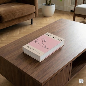 May include: A dark brown wooden coffee table with a book titled "PICASSO" on top. The book has a pink cover with a black line drawing and the text "MUSÉE D'ORSAY". The table has a lower shelf. The setting is a living room.
