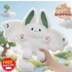 May include: A white plush toy shaped like a bunny with large, wing-like ears and wings. The ears have green inner linings, and the paws are pink. The toy has a small face with black dots for eyes and a curved mouth.