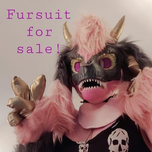 以下が含まれることがあります： モンスターのようなデザインのカラフルなファースーツ。マスクは黒と金で、ピンクのアクセント、鋭い白い歯、紫色の目があります。「Fursuit for sale!」というテキストが紫で表示されています。