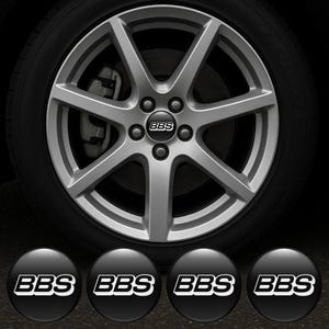 以下が含まれることがあります： 黒いタイヤに取り付けられた、マルチスポークデザインのシルバーアロイホイール。ホイールの中央には「BBS」のロゴがあります。4つの追加の黒と白のBBSロゴセンターキャップがホイールの下に表示されています。