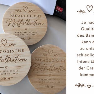 Op de afbeelding: Drie ronde bamboe onderzetters met een lasergegraveerde tekst die P&Auml;DAGOGISCHE Notfallration leest, gevolgd door F&Uuml;R ST&Auml;RKE, GEDULD UND GANZ VIEL HERZ. Elke onderzetter bevat decoratieve hart- en bladmotieven boven en onder de tekst.