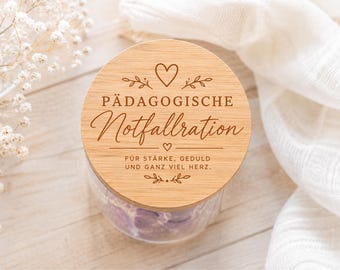 May include: A clear glass jar with a round wooden lid featuring a laser-engraved heart, floral accents, and the German text PÄDAGOGISCHE Notfallration FÜR STÄRKE, GEDULD UND GANZ VIEL HERZ. The jar contains purple items visible through the glass.