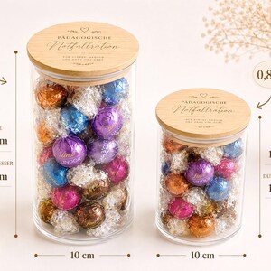 Op de afbeelding: Twee doorzichtige glazen potten met houten deksels gegraveerd met de tekst P&Auml;DAGOGISCHE Notfallration. De grotere pot heeft een inhoud van 1 liter, is 18 cm hoog en 10 cm in diameter. De kleinere pot bevat 0,8 liter, is 13 cm hoog en 10 cm in diameter.