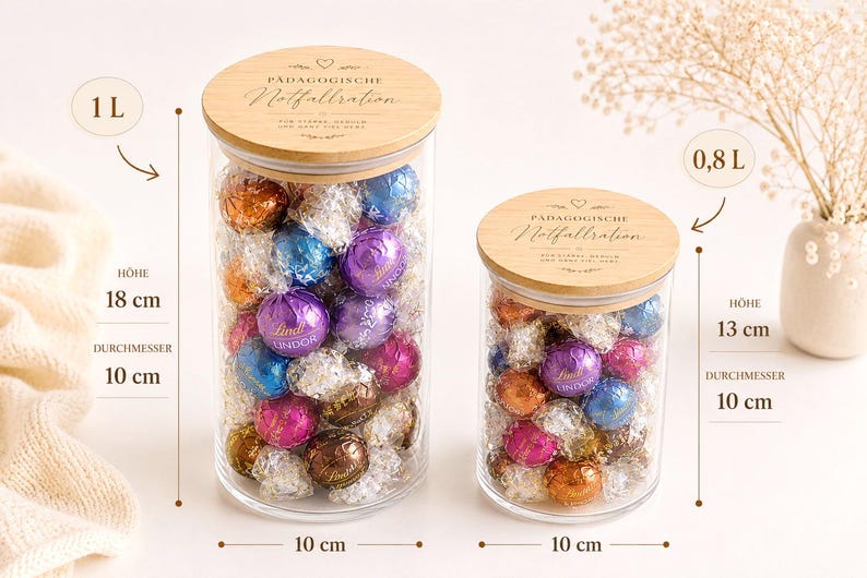 Op de afbeelding: Twee doorzichtige glazen potten met houten deksels gegraveerd met de tekst P&Auml;DAGOGISCHE Notfallration. De grotere pot heeft een inhoud van 1 liter, is 18 cm hoog en 10 cm in diameter. De kleinere pot bevat 0,8 liter, is 13 cm hoog en 10 cm in diameter.