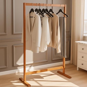 Op de afbeelding: Een houten kledingrek in minimalistische stijl, met een crèmekleurige blazer, een wit overhemd, een beige trui en een grijze broek. Het rek is gemaakt van lichtbruin hout en heeft een eenvoudig, functioneel ontwerp.