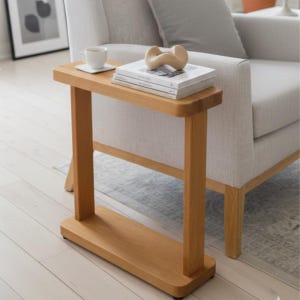 May include: A light-coloured wooden side table with a rectangular top and a lower shelf. The table has a minimalist design with a cup, coaster, books, and a decorative object on top. The table is approximately 71 cm tall.