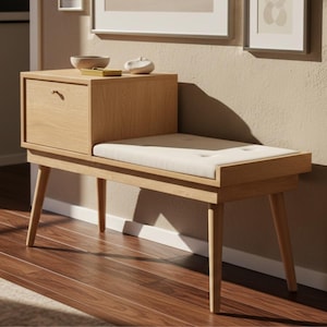 May include: A light-colored wooden entryway bench with a built-in drawer and a cushioned seat. The bench has four angled legs and a small drawer with a curved handle. The seat cushion is off-white and button-tufted. The bench is placed on a hardwood floor.