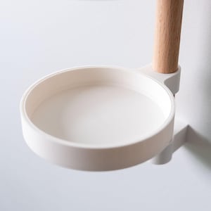 May include: A white, circular wall-mounted shelf with a wooden support. The shelf has a raised edge and is designed for small items. The wooden support is light brown. The shelf is made of a smooth, matte material, and is likely made of plastic.