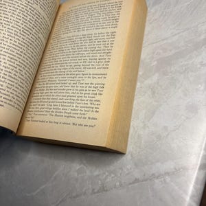 May include: An open book with yellowed pages, titled "Unfinished Tales." The text is in English, with a focus on the story. The book is on a light gray surface.