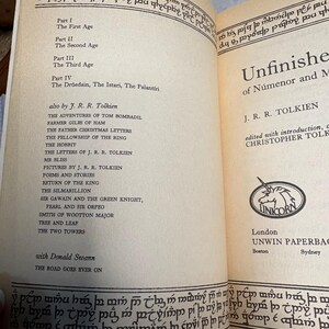 May include: Open book with the title "Unfinished Tales of N&uacute;menor and Middle-earth" by J.R.R. Tolkien. The book's table of contents is visible, listing various stories and essays. The cover features a Unicorn logo.