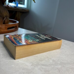 May include: A hardcover book titled "Unfinished Tales" by J.R.R. Tolkien. The book has a colorful cover with illustrations and gold-colored page edges. The book is lying on a white surface.