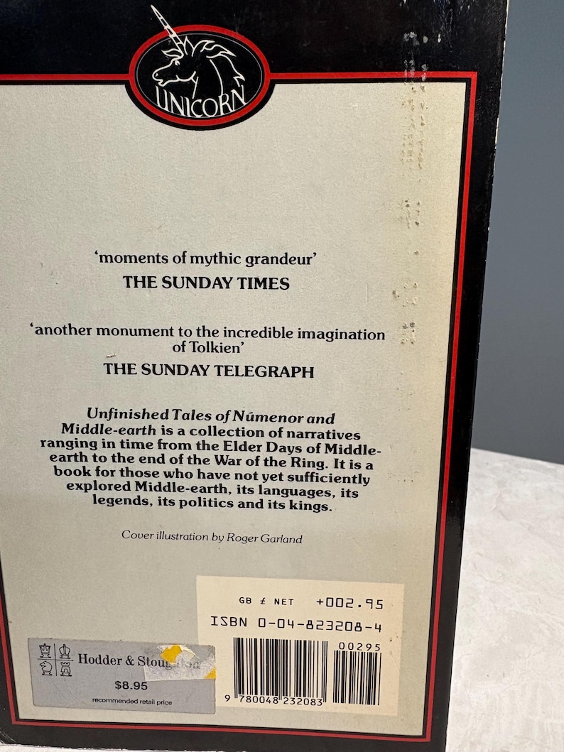 May include: The back cover of a book titled "Unfinished Tales of N&uacute;menor and Middle-earth." The cover features quotes from The Sunday Times and The Sunday Telegraph. The book is published by Unicorn and includes a barcode and ISBN.