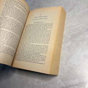 May include: An open book with yellowed pages, featuring text from "Unfinished Tales" and "Narn I Hin H&uuml;rin." The book's spine is visible, and the pages are slightly aged.
