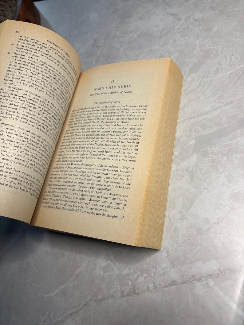 May include: An open book with yellowed pages, featuring text from "Unfinished Tales" and "Narn I Hin H&uuml;rin." The book's spine is visible, and the pages are slightly aged.