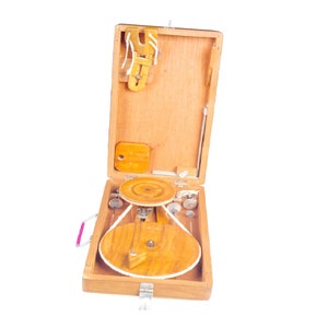May include: A wooden box with a hinged lid, containing a small wooden wheel and other tools. The box is open and the wheel is visible. The box has a pink handle.