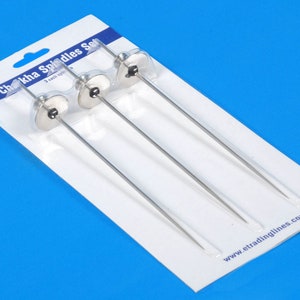 May include: A set of three Chokha spindles packaged on a white and blue card. Each spindle has a silver-colored metal disc and a long, thin, silver-colored metal rod. The packaging includes the text "Chokha Spindles Set" and "3 each spindles".