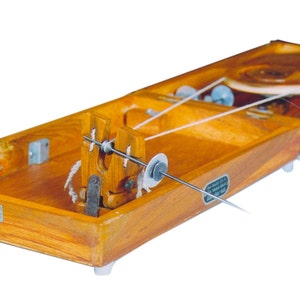 May include: A wooden spinning wheel with a white thread wound around it. The wheel is mounted on a wooden base with a small metal spindle.
