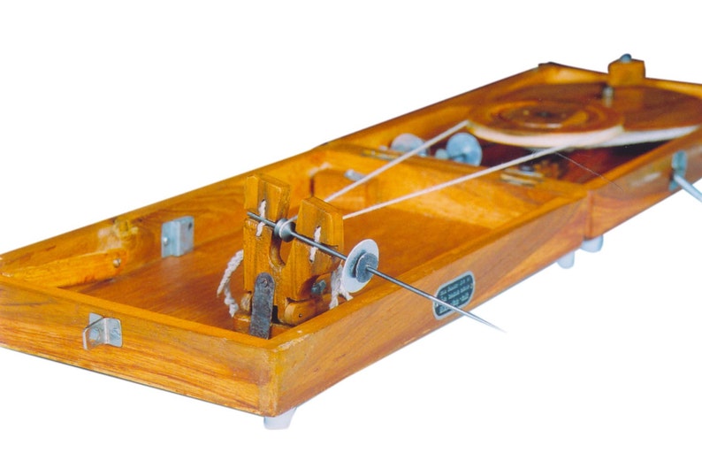 May include: A wooden spinning wheel with a white thread wound around it. The wheel is mounted on a wooden base with a small metal spindle.