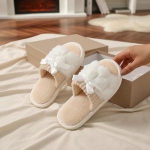 Pu&ograve; includere: Un paio di pantofole color crema, in peluche, con una parte superiore soffice e un piccolo fiocco bianco. Le pantofole hanno un interno beige chiaro e sono presentate con una confezione regalo.