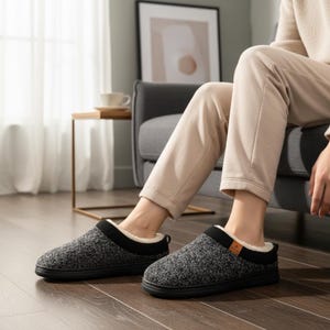 May include: Gray and black knit slippers with a black trim and a faux fur lining. The slippers have a rubber sole and a small brown tag on the side. The slippers are designed for indoor use and provide comfort and warmth.