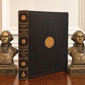 Peut inclure: Un livre relié noir intitulé History of Freemasonry Illustrated, flanqué de deux bustes identiques de couleur bronze représentant George Washington portant des tabliers maçonniques. Le dos du livre présente des lettres et symboles dorés.