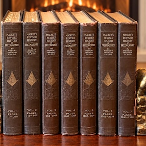 Könnte beinhalten: Ein siebenteiliges Set von Mackey's Revised History of Freemasonry von Robert Ingham Clegg, gebunden in dunkelbraunen Einbänden mit goldener Schrift und Symbolen, gehalten von zwei bronzefarbenen Buchstützen, die eine sitzende Figur darstellen.