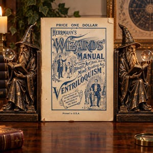 Pode incluir: Dois suportes para livros de feiticeiro cor de bronze com figuras de chapéus pontiagudos segurando livros abertos e esferas de cristal, ladeando um livro intitulado Herrmann's Wizards' Manual, Secrets of Magic Art, Mind Reading Art and Ventriloquism.