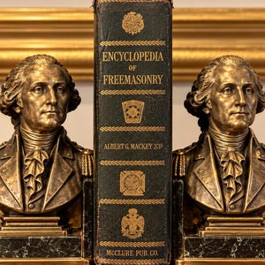 Könnte beinhalten: Zwei bronzefarbene Büsten von George Washington flankieren ein schwarzes Buch mit dem Titel Encyclopedia of Freemasonry von Albert G. Mackey 33. Die Büsten zeigen detaillierte Militäruniformen mit Epauletten auf dunkelgrünen Marmorsockeln.