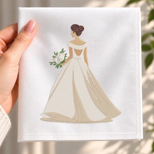 Könnte beinhalten: Eine weiße Stoffserviette mit einer Stickerei, die eine Figur in einem langen, schulterfreien Kleid mit tiefem Rückenausschnitt zeigt. Die Figur hat braunes Haar in einem Dutt und hält einen Strauß aus weißen Blumen mit grünen Blättern.