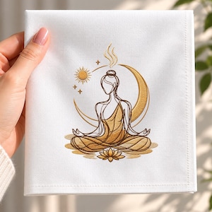 May include: A white square cloth napkin featuring a gold embroidered line art design of a person in a seated meditation pose. The embroidery includes a crescent moon, a sun, small stars, and a lotus flower at the base in shades of gold thread.