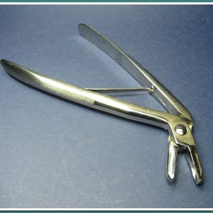 Peut inclure: Un instrument chirurgical en acier inoxydable, une pince, est posé sur une surface bleue. La pince a une conception articulée avec des poignées incurvées et une pointe de préhension. Le métal a une surface polie et réfléchissante.