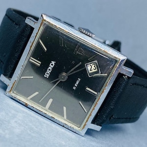 Puede incluir: Un reloj de pulsera Sekonda vintage con caja cuadrada plateada y esfera negra. El reloj tiene una visualización de fecha a las 3 en punto y una correa de cuero negro. La esfera tiene agujas e indicadores plateados. Un reloj clásico.