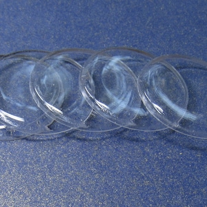 May include: Five clear glass watch crystals, stacked on top of each other, on a blue background.