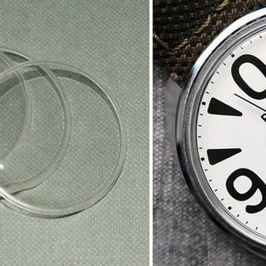 Peut inclure: Un ensemble de quatre verres de montre transparents et une montre Raketa vintage. La montre a un cadran blanc avec de grands chiffres noirs et la marque "Raketa". Les aiguilles de la montre sont noires, et la montre est sur un bracelet à motifs.