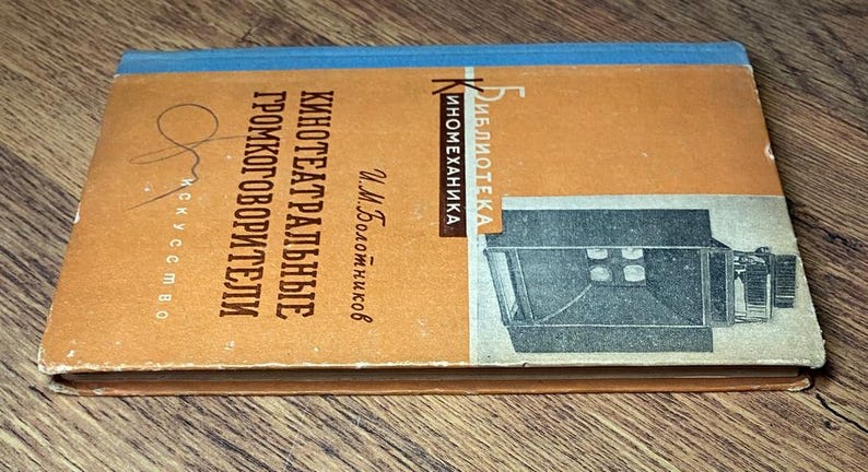 May include: A vintage book with a tan cover and blue spine, titled in Russian. The cover features text and an illustration of a projector. The book is titled "Theater Speakers" and is part of the "Inomekhanika" library.