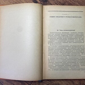 May include: An open vintage book with aged, yellowed pages. The right page features Cyrillic text under the heading "CHAPTER 1" and "GENERAL INFORMATION ABOUT LOUDSPEAKERS." The book's cover is a faded orange color, and the pages are slightly curled.