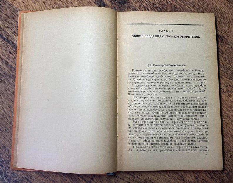 May include: An open vintage book with aged, yellowed pages. The right page features Cyrillic text under the heading "CHAPTER 1" and "GENERAL INFORMATION ABOUT LOUDSPEAKERS." The book's cover is a faded orange color, and the pages are slightly curled.