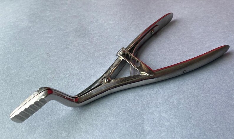 K&ouml;nnte beinhalten: Silberfarbenes medizinisches Instrument mit gebogenem Griff und zwei gegen&uuml;berliegenden Klingen. Das Instrument hat einen Scharniermechanismus und einen strukturierten Griff. Die Klingen haben eine rote Innenseite.