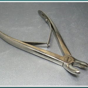 Peut inclure: Une paire de pinces chirurgicales argentées avec une poignée incurvée et une petite vis sur le côté.