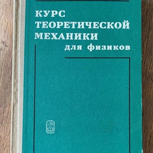May include: A teal-colored book with the title "Курс теоретической механики для физиков" in white Cyrillic lettering. The book has a beige spine and a small emblem at the bottom. The author's name, И.И.Ольховский, is at the top.
